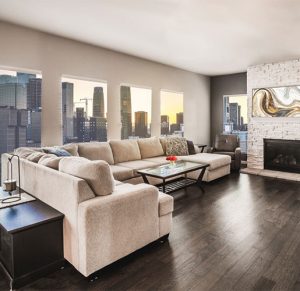 Living room with beige sectional couch in front of large windows with a skyline view